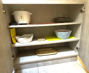 A kitchen cabinet with shelves containing a white pot, a blue patterned bowl, a yellow napkin, and a white cloth bag. - Aparts4Days 1-Bedroom Loft in Downtown Miraflores Near the Malecón (Miraflores)