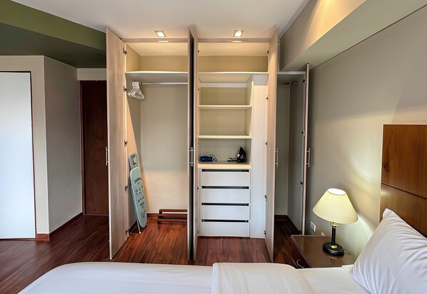 Une chambre d’hôtel comprenant un lit, une table de chevet avec une lampe, une armoire avec un miroir et une porte donnant sur une autre pièce.