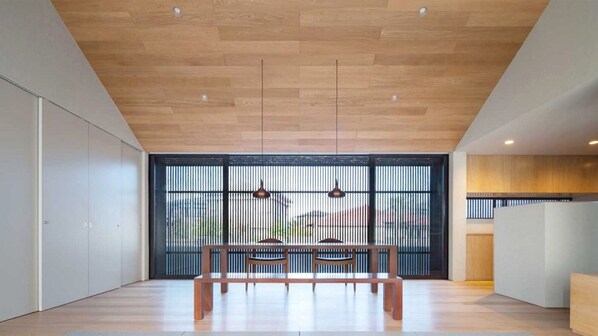 Un interior moderno con techo de madera, un banco y un amplio ventanal con persianas verticales.