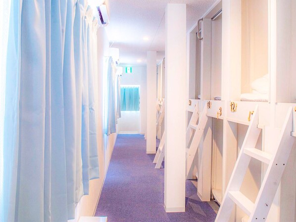 Un couloir d’hôtel aux murs blancs, avec une moquette violette et une rangée de casiers blancs numérotés.