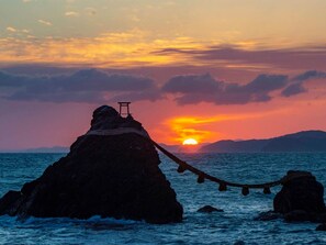 Un coucher de soleil sur l’océan, avec une formation rocheuse et une petite construction au sommet.