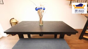 A dining table with a bench, a vase with dried plants, and a logo for JB stays.