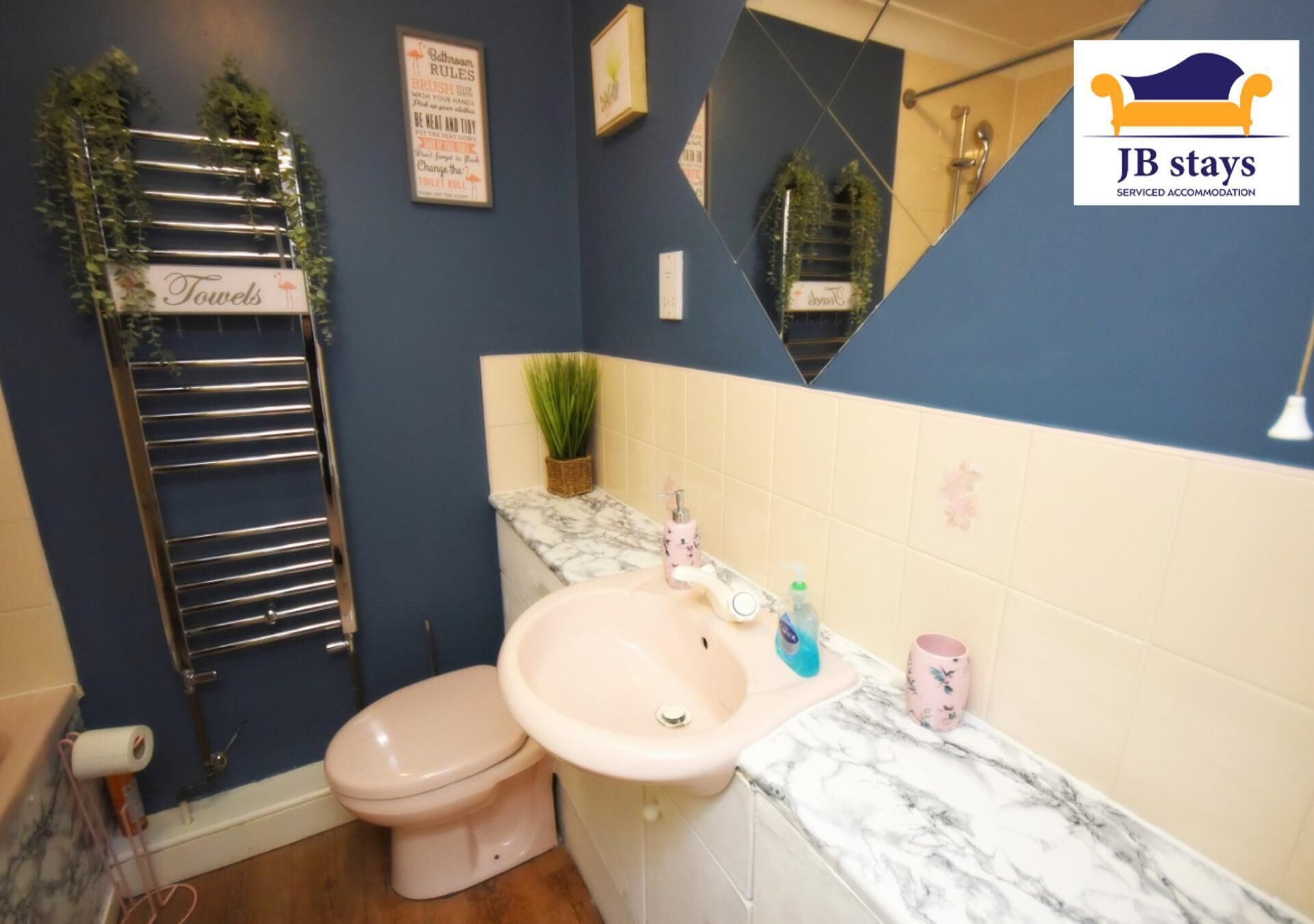 A bathroom with a pink sink, a toilet, a towel rack, and a mirror.