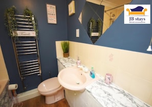 A bathroom with a pink sink, a toilet, a towel rack, and a mirror.