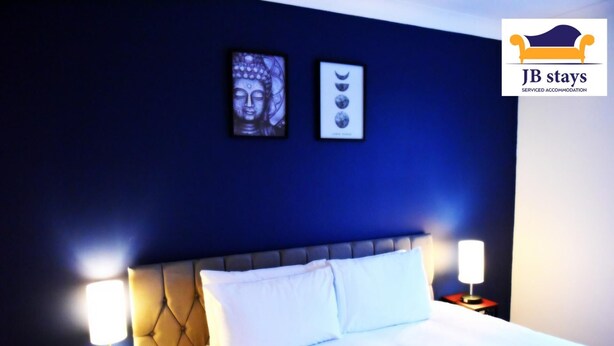 A hotel room with a large bed, two bedside lamps, a headboard, and two framed pictures on the wall.