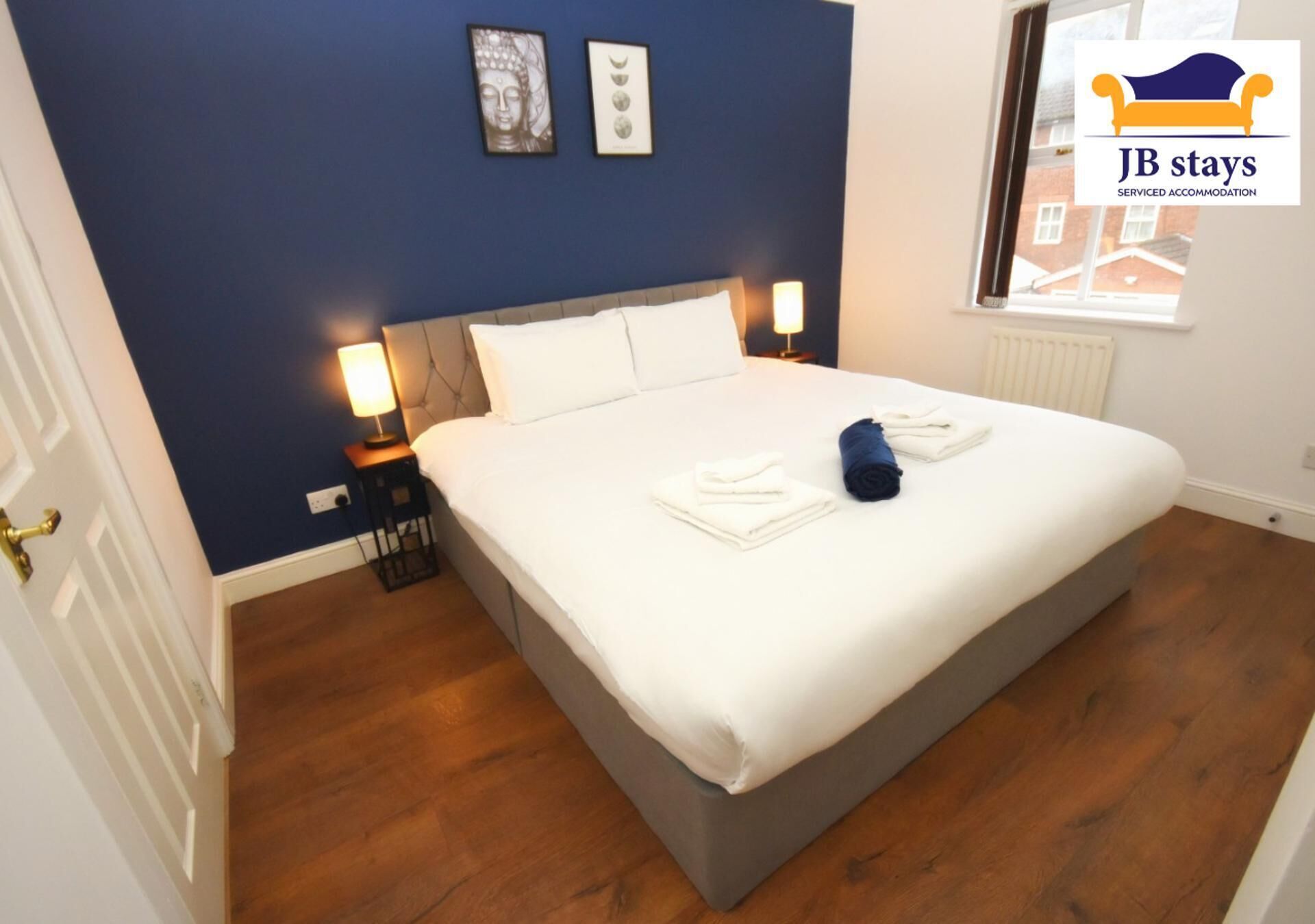 A neatly made bed in a room with blue walls, a wooden floor, and two bedside lamps.