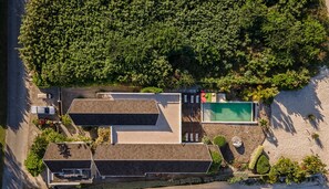 Vue aérienne d’une propriété dotée d’une piscine, de deux grands bâtiments et d’une forêt dense qui entoure le site.