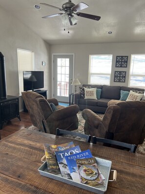A living room with a fireplace, a TV, and a dining table with magazines. - Cozy Cabin (Red River)