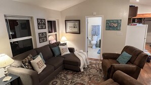 A living room with a brown sofa, a patterned rug, and a door leading to a bathroom. - Cozy Cabin (Red River)