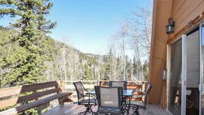 A wooden deck with outdoor furniture, including a bench and tables, overlooking a forested area. - Cozy Cabin (Red River)