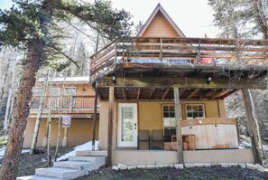 Enjoy the serene surroundings from the upper-level balcony of this cozy cabin, featuring a front door with a glass panel and a small porch area with a bench.