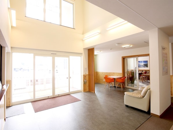 A spacious hotel lobby with a high ceiling, a seating area with a sofa and chairs, a small table, and a large sliding glass door leading to an outdoor area.