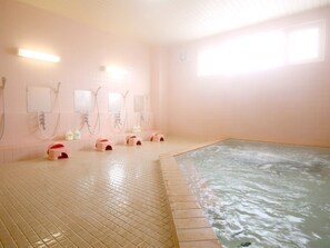 Un área de spa con hidromasaje, suelo de baldosas y duchas empotradas en la pared.
