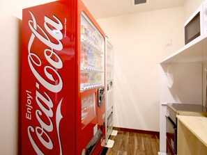 Una cocina compacta con una máquina expendedora roja de Coca-Cola, un microondas y una encimera de madera.