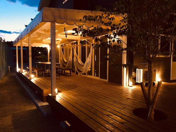 An outdoor wooden deck with a covered seating area, a tree, and a building in the background.