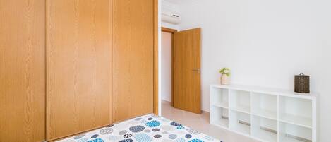 Una stanza con armadi in legno, un tappeto decorato, un tavolino consolle bianco con una pianta e una libreria bianca.