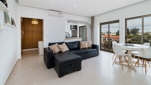 Ein modernes Wohnzimmer mit einer schwarzen Eckcouch, einem Esstisch mit Stühlen und großen Fenstern mit Blick auf die Stadt.