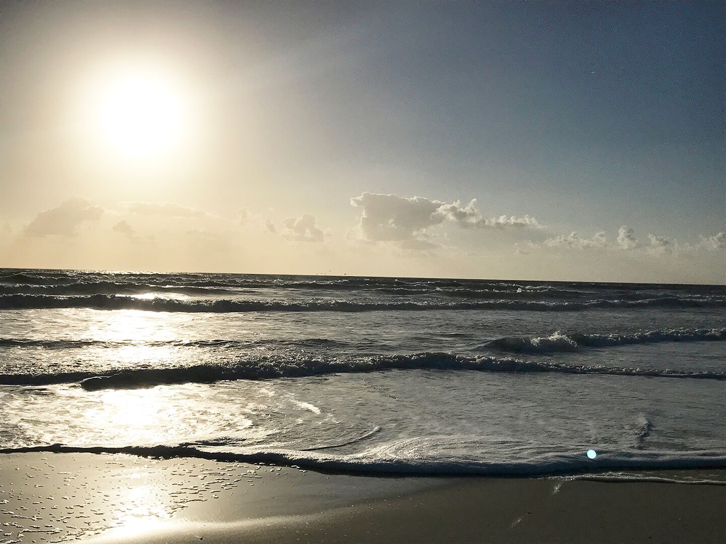 Una playa con olas y el sol brillando.