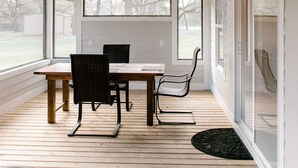 A covered patio with a table and chairs, wooden flooring, and a ceiling fan.