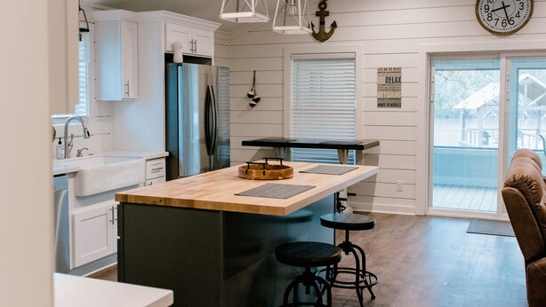 A modern kitchen with white cabinetry, a wooden island, and a large clock on the wall.