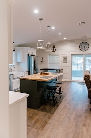 A modern kitchen with white cabinetry, a wooden island, and a large clock on the wall.