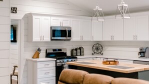 A modern kitchen with white cabinetry, a central island, stainless steel appliances, and pendant lighting.