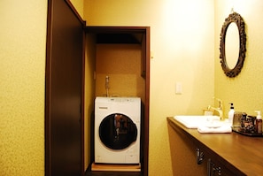 A compact laundry room with a washing machine, a sink, and a mirror on the wall.