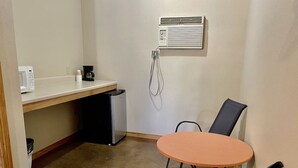 Eine kleine Küchenzeile mit Mikrowelle, Kaffeemaschine und Kühlschrank. Es gibt einen runden orangefarbenen Tisch mit zwei Stühlen und einen Duschkopf an der Wand.