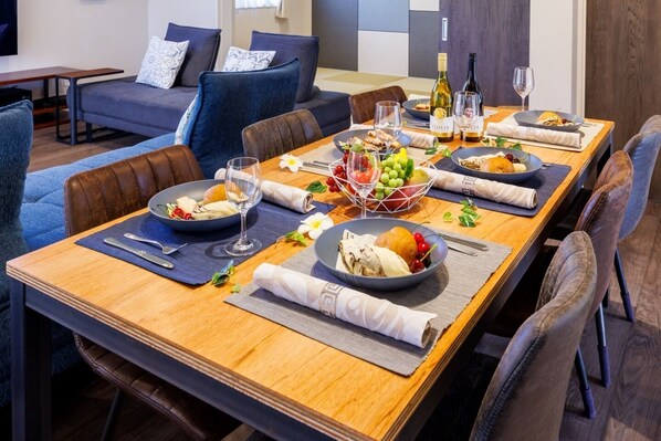A dining area with a long wooden table set for a meal, surrounded by blue upholstered chairs.