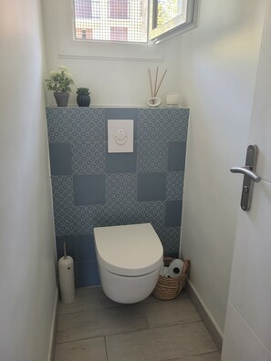 Ein kleines Badezimmer mit Toilette, gemusterten Fliesen, einem Fenster und einer Tür.