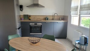 A modern kitchen with a round wooden table, green chairs, a built-in oven, and a window with curtains. - T2 near historic center (Manosque)