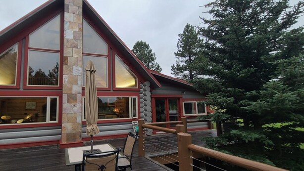 A log cabin-style building with large windows, a wooden deck, and a stone pillar. - Spacious cabin in Angel Fire area - 6 miles to ski slopes and recreation area (Angel Fire)