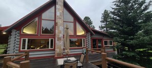 A log cabin-style building with large windows, a wooden deck, and a stone pillar.