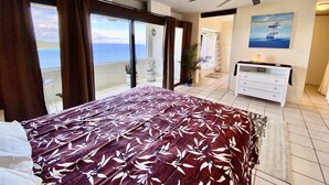 Une chambre avec un lit, un ventilateur de plafond, une commode et une vue sur l’océan.