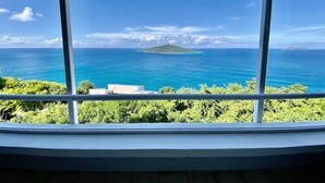 Une vue depuis une fenêtre donnant sur une mer turquoise et une petite île.
