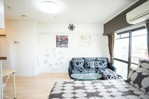 A modern living room with a sofa, a coffee table, and a bed with a patterned bedspread.