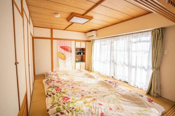A traditional Japanese-style room with tatami flooring, a low wooden ceiling, and a large bed with floral bedding.