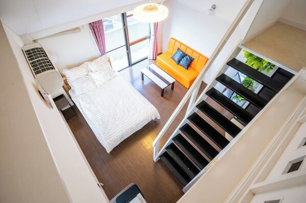 A bedroom with a bed, a white heater, a window with curtains, an orange sofa, and a staircase.