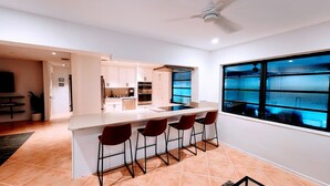 A modern kitchen with a central island, bar stools, and a large window with blue-tinted glass. - Boca Raton Home with private heated pool, close to FAU, Beach & Mizner! (Boca Raton)