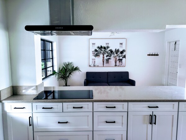 A kitchen with white cabinets, a black countertop, a stove, and a wall-mounted exhaust hood. - Boca Raton Home with private heated pool, close to FAU, Beach & Mizner! (Boca Raton)