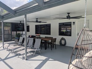 A covered patio area with a table and chairs, ceiling fans, and a hanging chair. - Boca Raton Home with private heated pool, close to FAU, Beach & Mizner! (Boca Raton)