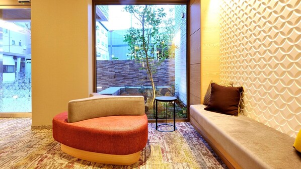 A modern hotel room with a curved red and beige sofa, a small round table, and a patterned carpet.