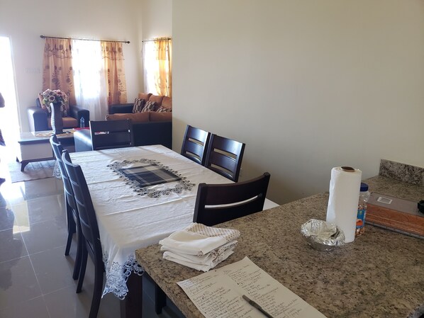 A dining area with a table set for four, a bench, and a small kitchen counter with a roll of paper towels and a jar.
