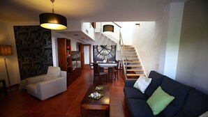Een ruime woonkamer met een trap, een piano en een grote wandklok.