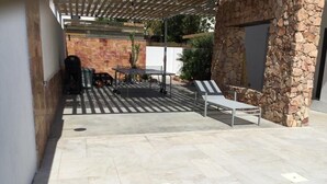 Een terras buiten met een zwembad, een stenen muur en lounge stoelen.