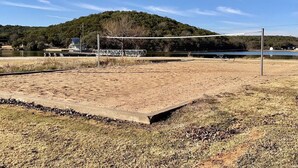 Ein Sandvolleyballfeld mit einem Metallzaun, einer Bank und einem kleinen Gebäude im Hintergrund.