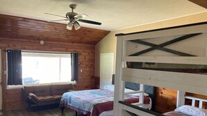 Eine Holzhütte mit Deckenventilator, einer Couch und Stockbetten.