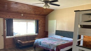 Ein Schlafzimmer mit Holzbalkendecke, einem Bett mit Quilzudecke, einem Fenster mit Vorhängen und einem Holzboden.
