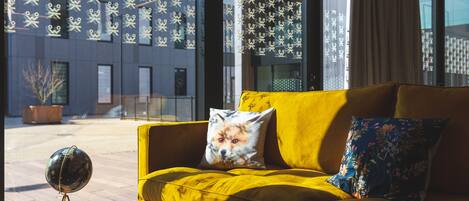 A yellow sofa with a fox-themed pillow and a globe on a tripod stand in a modern room with large windows and patterned curtains.