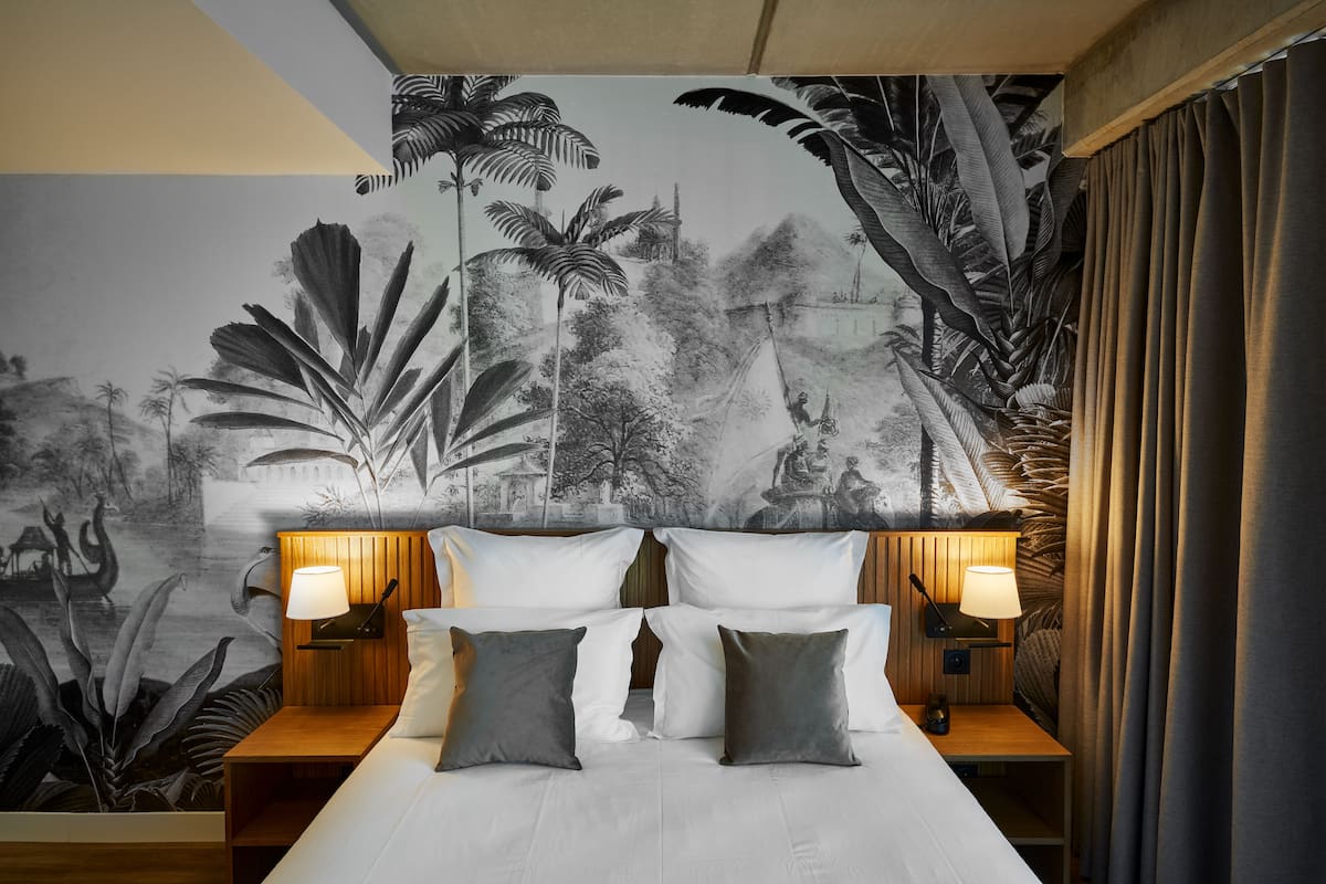 A hotel room with a large bed, two bedside tables with lamps, and a mural of a tropical scene on the wall.